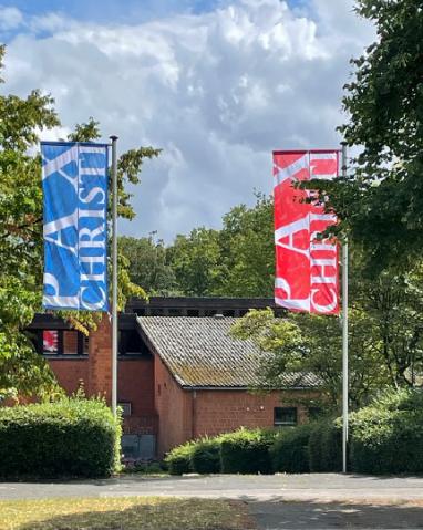Blick von draußen auf Pax Christi mit roter und blauer Fahne
